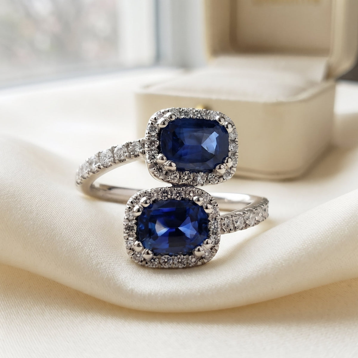 Blue sapphire and diamond double halo crossover ring in platinum on ivory silk