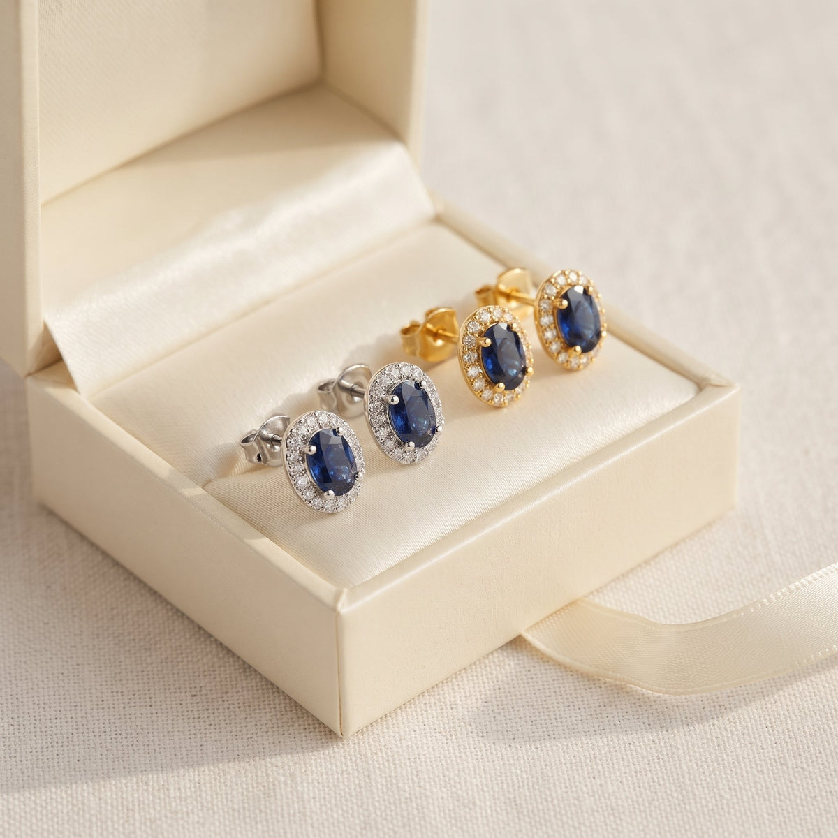 Oval blue sapphire and diamond halo earrings in 18k white gold and 18k yellow gold in an open gift box