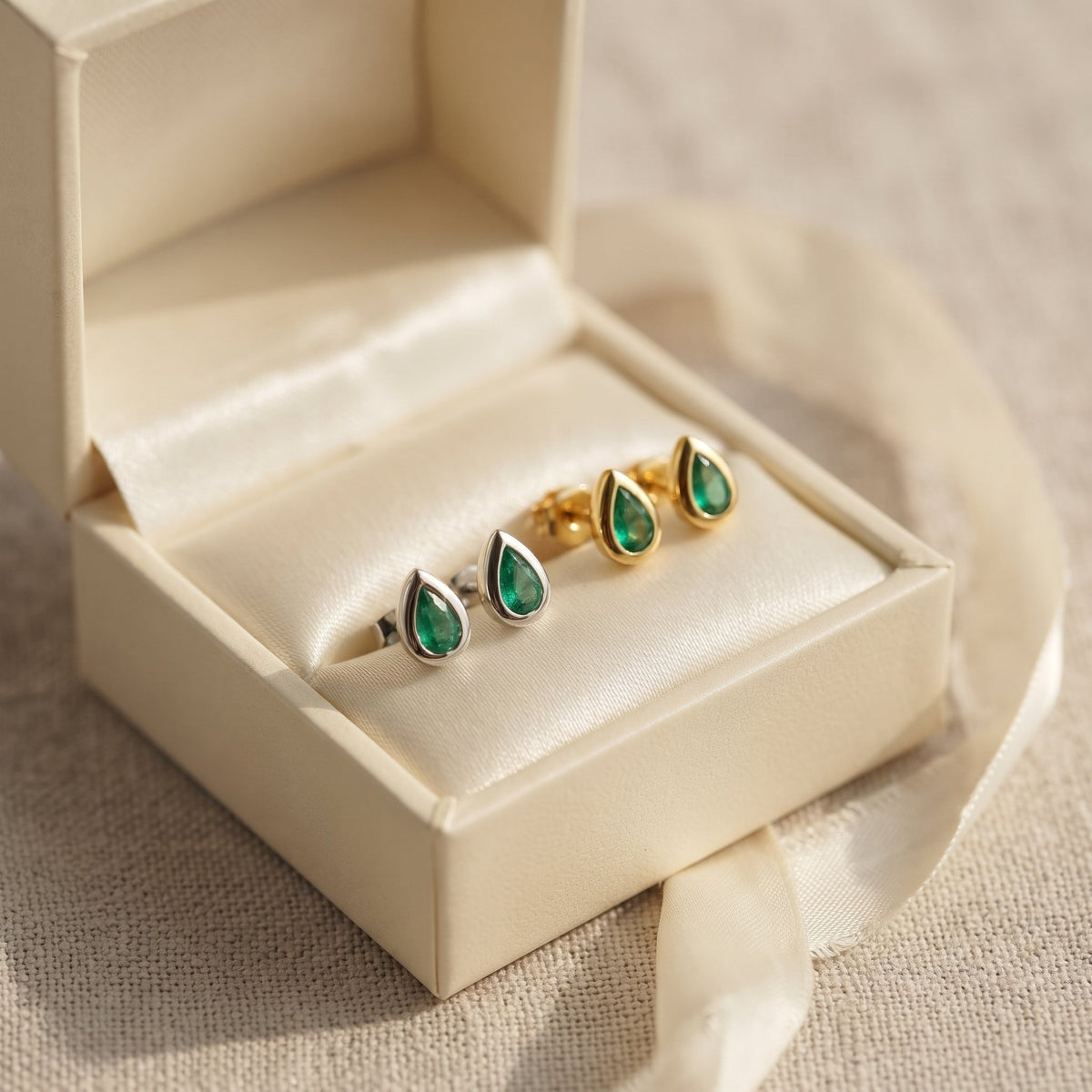 Pear emerald rubover stud earrings in 18k white gold and 18k yellow gold in an open gift box