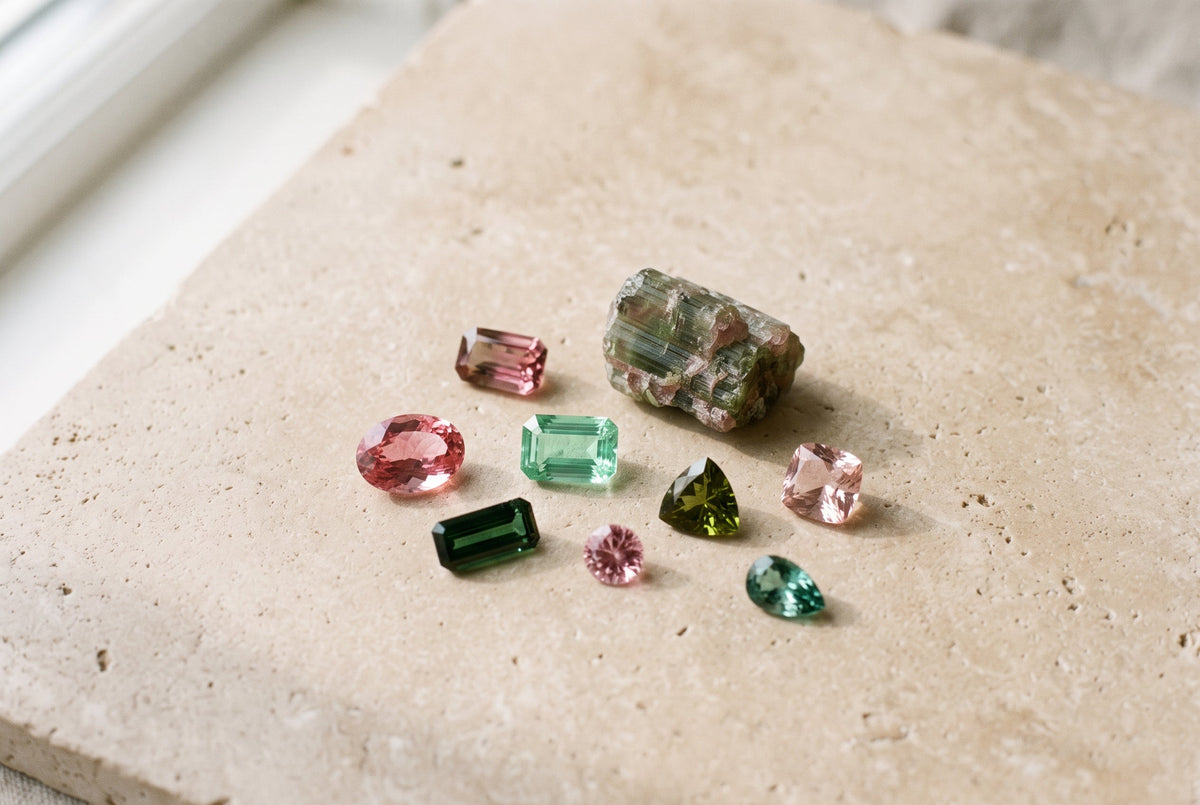 Loose pink and green tourmaline gemstones on a beige stone surface