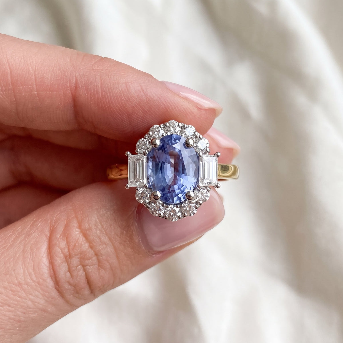 Purple sapphire and diamond oval halo ring in 18k yellow gold and platinum, held between the fingers