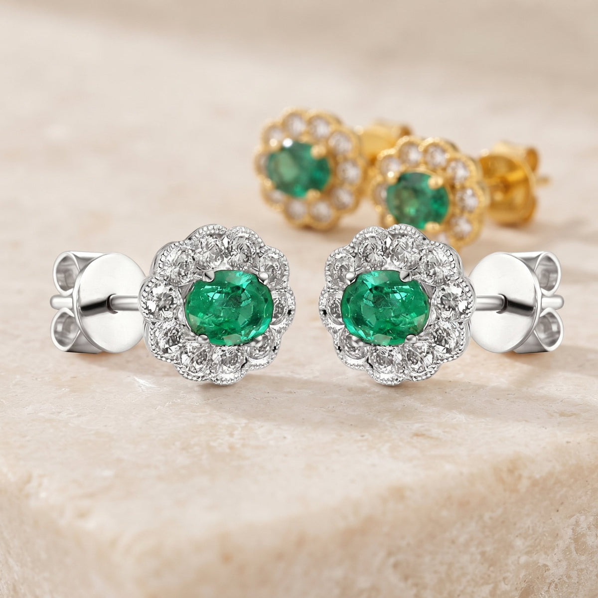 Oval emerald and diamond milgrain cluster earrings in 18k white gold and 18k yellow gold on a cream stone