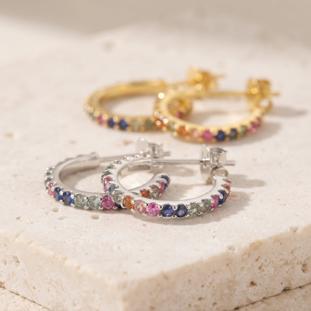 Rainbow sapphire hoop earrings in 18k white gold and 18k yellow gold on a cream stone
